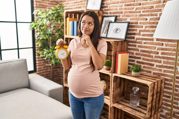 Young Pregnant Woman Holding Alarm Clock Due Date Serious Face — Φωτογραφία Αρχείου