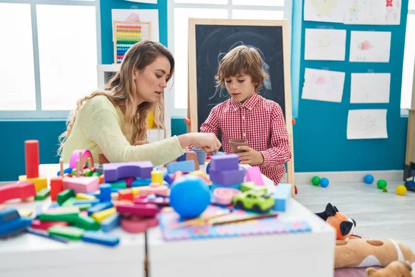 Teacher and toddler playing with geometry blocks sitting on table at kindergarten