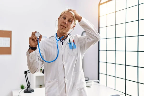 Młody Blondyn Noszący Mundur Lekarza Trzymający Stetoskop Klinice Zestresowany Sfrustrowany — Zdjęcie stockowe