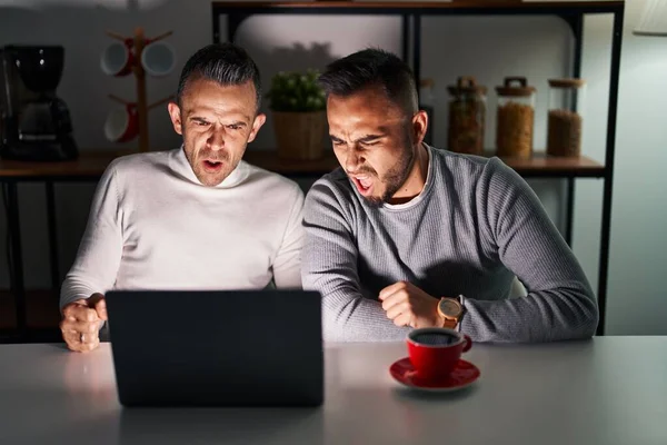 Homosexual couple using computer laptop angry and mad screaming frustrated and furious, shouting with anger. rage and aggressive concept.