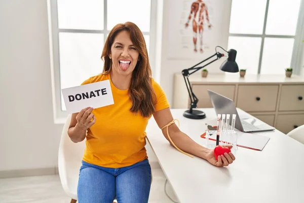 Hispanic woman supporting blood donation sticking tongue out happy with funny expression.