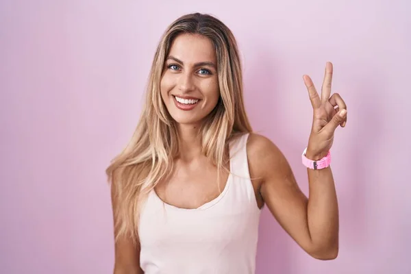 Молодая Блондинка Стоит Розовом Фоне Показывая Показывая Пальцами Номер Два — стоковое фото