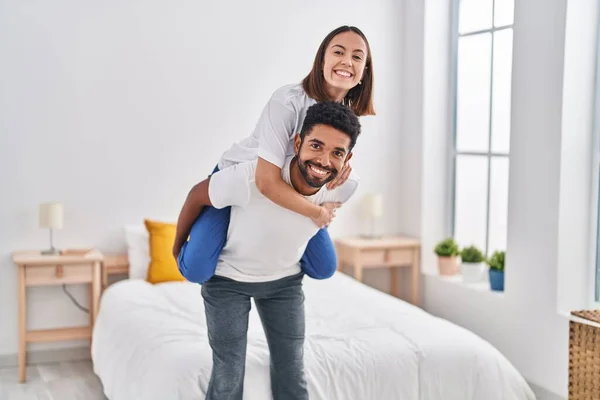 Man and woman smiling confident holding girlfriend on back at bedroom