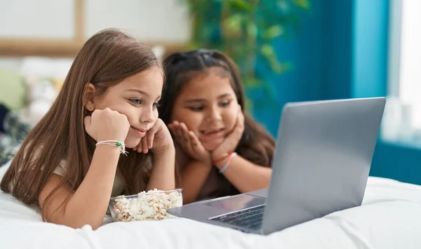 Two kids watching movie on laptop lying on bed at bedroom