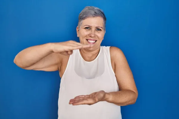 中年的高加索女人站在蓝色的背景上 手举着大号和大号的手势 测量符号 微笑着看着摄像机 计量概念 — 图库照片