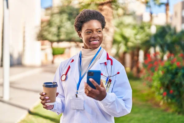 African American Woman Wearing Doctor Uniform Using Smartphone Drinking Coffee — Stockfoto