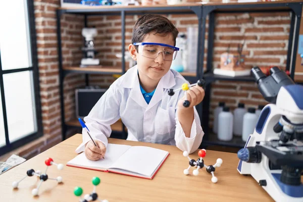 Adorable Hispanic Boy Student Writing Notebook Holding Molecules Laboratory Classroom — Stock Photo, Image