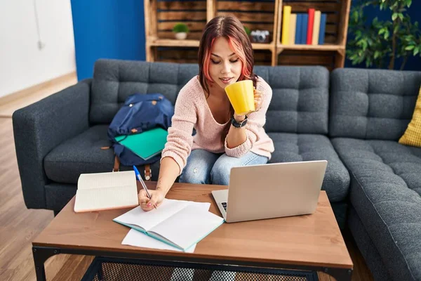 若いですCaucasian女性学生座っています上のソファ書きノートブック飲料コーヒーに自宅 — ストック写真