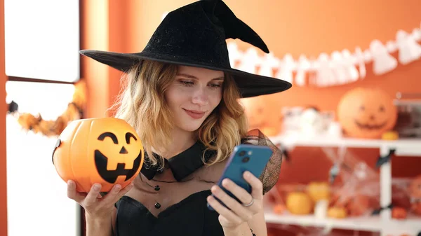 Young Blonde Woman Holding Halloween Pumpkin Basket Using Smartphone Home — Foto de Stock