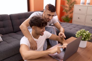 Two hispanic men couple using laptop sitting on sofa at home