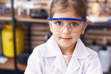 Adorable hispanic girl scientist student smiling confident at laboratory classroom