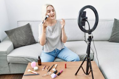 Beyaz bir kadın evde fırça kullanırken görüntülü konuşma yapıyor.