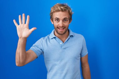 Caucasian man standing over blue background showing and pointing up with fingers number five while smiling confident and happy. 