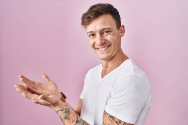 Pembe arka planda duran beyaz bir adam avuçları açık bir şekilde fotokopi alanını gösteriyor, gülümseyerek mutlu bir şekilde gülümsüyor. 