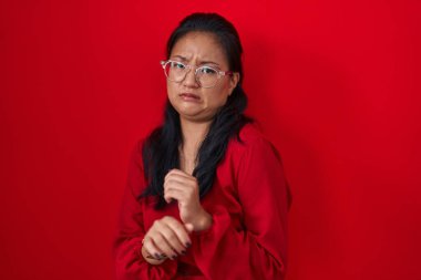 Asian young woman standing over red background disgusted expression, displeased and fearful doing disgust face because aversion reaction. 
