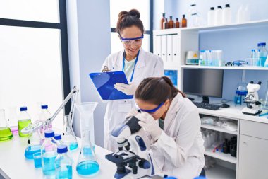 Woman and girl wearing scientist uniform using microscope at laboratory