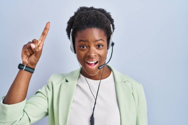 African american woman wearing call center agent headset smiling amazed and surprised and pointing up with fingers and raised arms. 