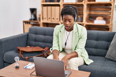 African american woman doing online session at consultation office scared and amazed with open mouth for surprise, disbelief face 
