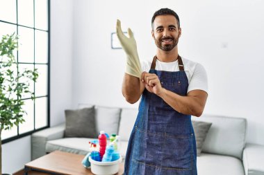 Önlük giyip evde eldiven temizleyen kendine güvenen İspanyol genç adam.
