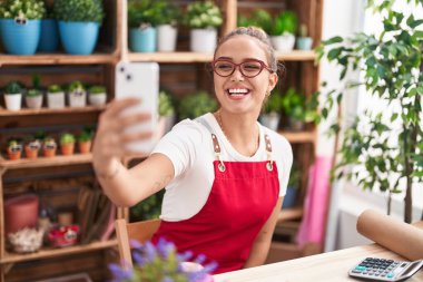 Young beautiful hispanic woman florist make selfie by smartphone at florist