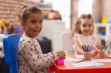 Two kids preschool students sitting on table drawing on paper at kindergarten