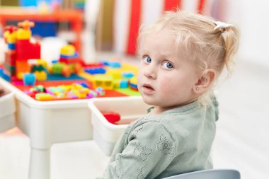 Adorable blonde girl playing with construction blocks sitting on table at kindergarten