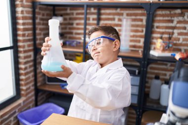 Adorable hispanic boy student holding test tube at laboratory classroom