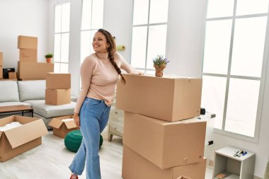 Genç, güzel, İspanyol bir kadın yeni evinde kendine gülerek duruyor.