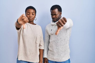 Genç Afro-Amerikan çifti birlikte mavi arka planda dikiliyorlar mutsuz ve kızgın görünüyorlar reddediliyorlar ve olumsuz davranıyorlar. kötü ifade. 