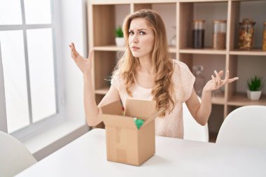 Beautiful blonde woman with cardboard box shouting and screaming loud to side with hand on mouth. communication concept. 