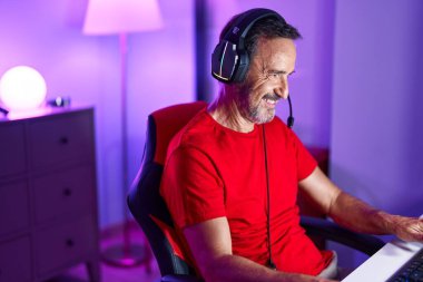 Middle age man streamer playing video game using computer at gaming room