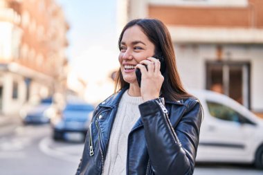Gülümseyen genç bir kadın caddedeki akıllı telefondan konuşuyor.