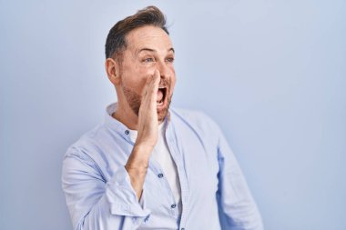 Orta yaşlı, beyaz bir adam mavi arka planda durmuş el ele tutuşarak bağırıyor ve çığlık atıyordu. iletişim konsepti. 