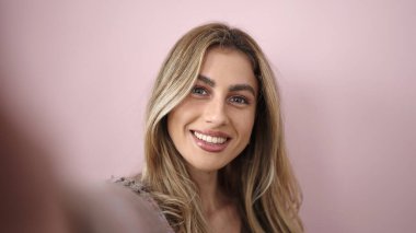 Young blonde woman smiling confident making selfie by camera over isolated pink background