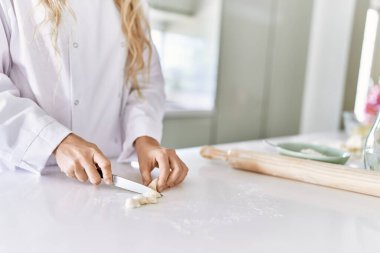 Young woman wearing cook uniform cutting dough at kitchen