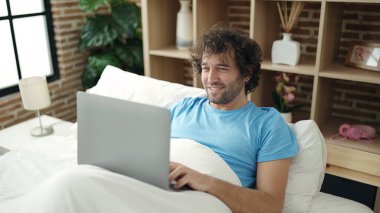 Genç İspanyol adam yatak odasında dizüstü bilgisayar kullanıyor.