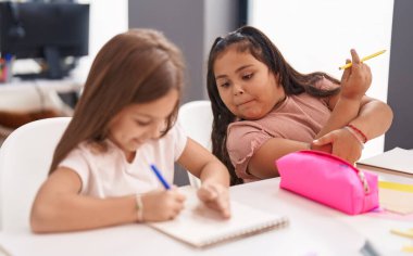 Two kids students sitting on table drawing on notebook paper at classroom