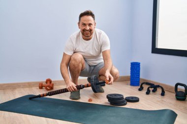 Genç beyaz adam gülümsüyor. Spor merkezinde spor yapmak için barlara ve disklere hazırlanıyor.