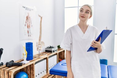 Klinikte çalışan, fizyoterapist üniforması giyen beyaz bir kadın.