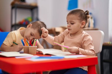 Two kids preschool students sitting on table drawing on paper at kindergarten