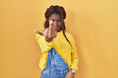 African woman standing over yellow background showing middle finger, impolite and rude fuck off expression 
