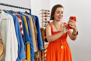 Orta yaşlı İspanyol kadın perakende dükkanında akıllı telefon kullanarak gülümsüyor.