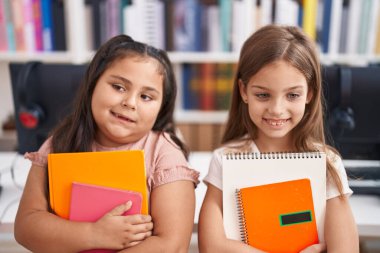 Two kids students smiling confident holding books at classroom