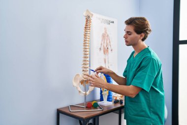 Young caucasian man physiotherapist touching anatomical model of spinal column at rehab clinic