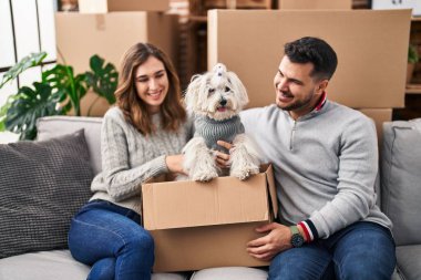 Man and woman smiling confident sitting on sofa with dog at new home