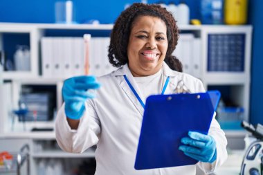 African american woman scientist reading document holding test tube at laboratory