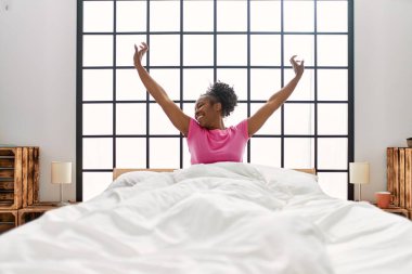 Afrikalı Amerikalı bir kadın yatak odasında kollarını açarak uyanıyor.