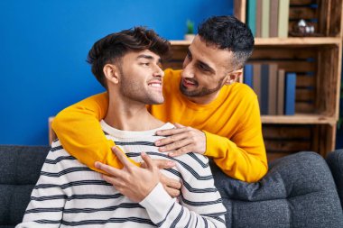 İki erkek, evdeki kanepede oturup birbirlerine sarılıyorlar.
