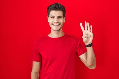 Young hispanic man standing over red background showing and pointing up with fingers number four while smiling confident and happy. 