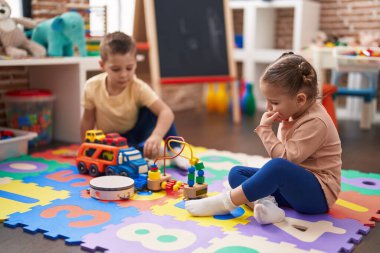 Two kids playing with cars toy sitting on floor at kindergarten